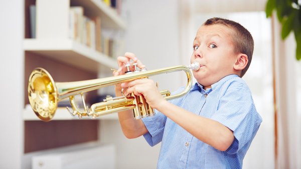 Kleiner Junge spielt Trompete und schaut dabei in der Kamera