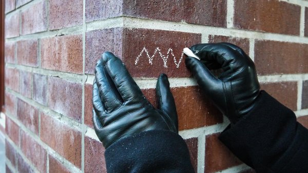Behandschuhte Hände schreiben Kreidezeichen an eine Hauswand