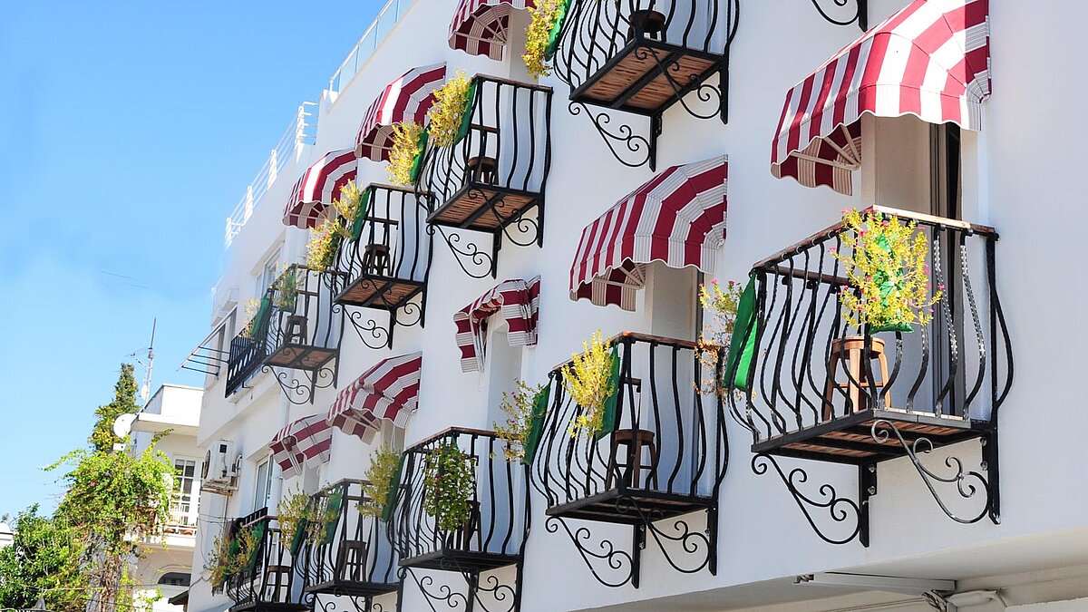 Viele kleine Balkone mit Markisen nebeneinander an einer sonnigen Hauswand